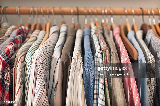 A variety of shirts hanging on a wooden clothes rack.