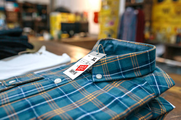 Close up of label with discount price over a blue plaid shirt on vintage store. Sales season and black friday concept. Organized apparel stacks ready to sell on clothes shop with industrial style.